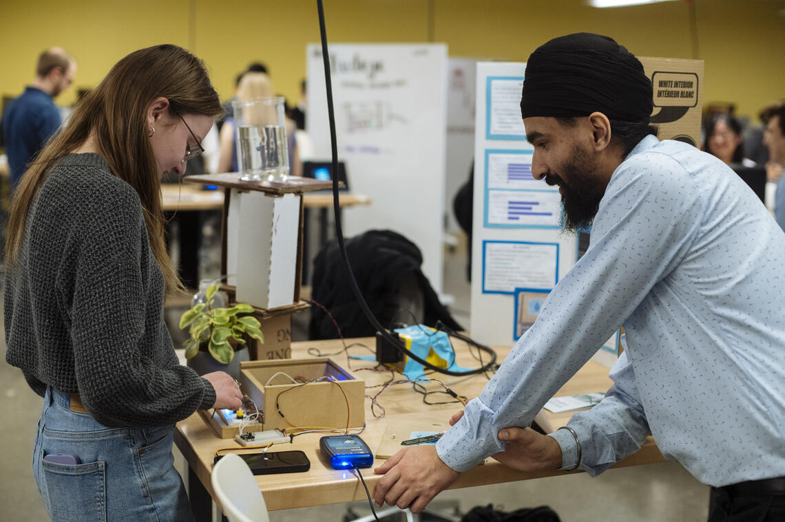 Two young students set up a demonstration of an electronic device in a classroom.