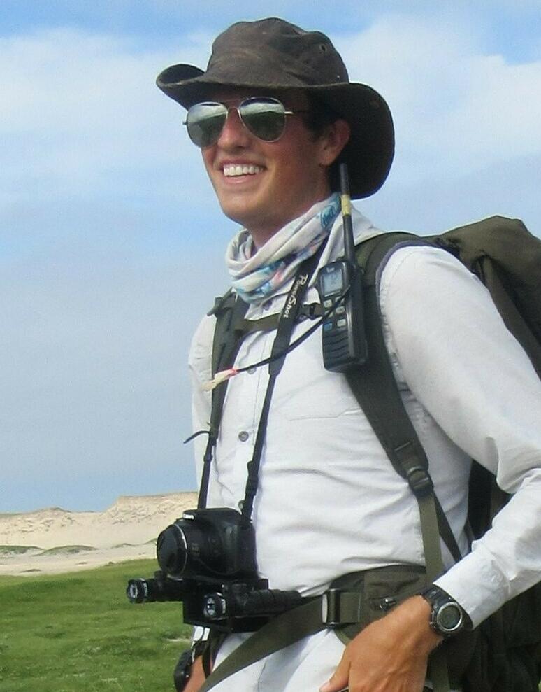 A man wearing a backpack and hat standing in a field