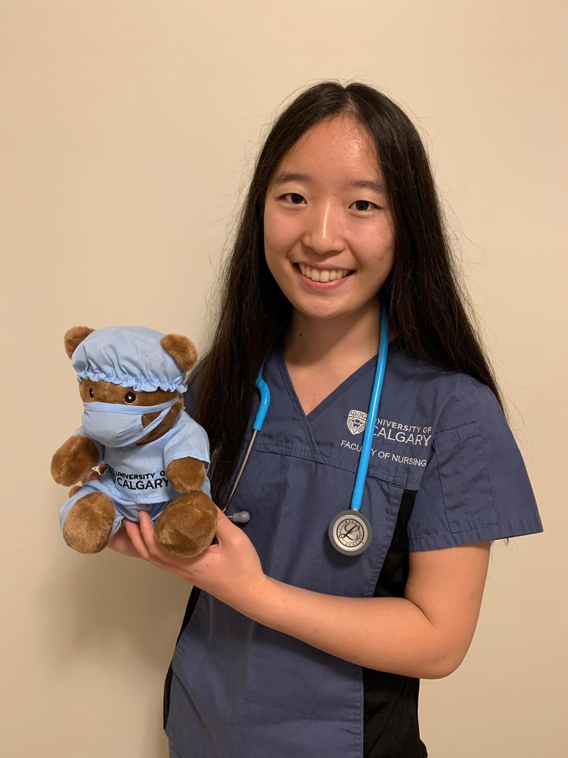 Cynthia dressed in her student nurse scrubs holds teddy bear also dressed in blue scrubs