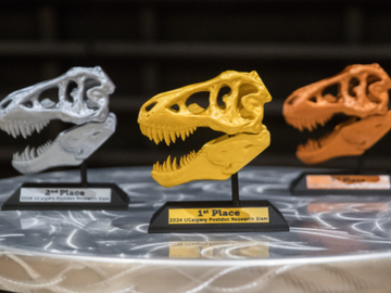 Pictures of silver, gold, and bronze t-rex skull trophies on a table