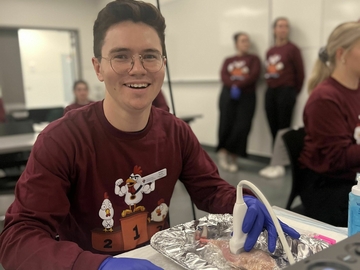 Student wearing nitrile gloves with an ultrasound probe and chicken vascular phantom model during SVECCS Chicken Phantom Olympics