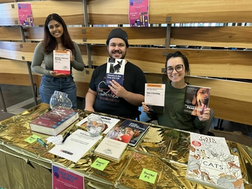 Three students pose with books at the WIDE Book Sale