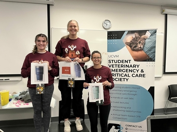 Three veterinary students on a podium holding their prizes won during the Chicken Phantom Competition,